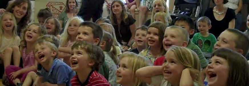 Preschool children and families laughing loudly at The Stupendous Mr. Magichead show.