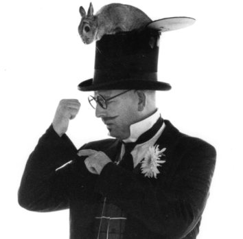 Kid's magician Mr. Magichead looking up his sleeve for a bunny which is coming out the top of his hat.